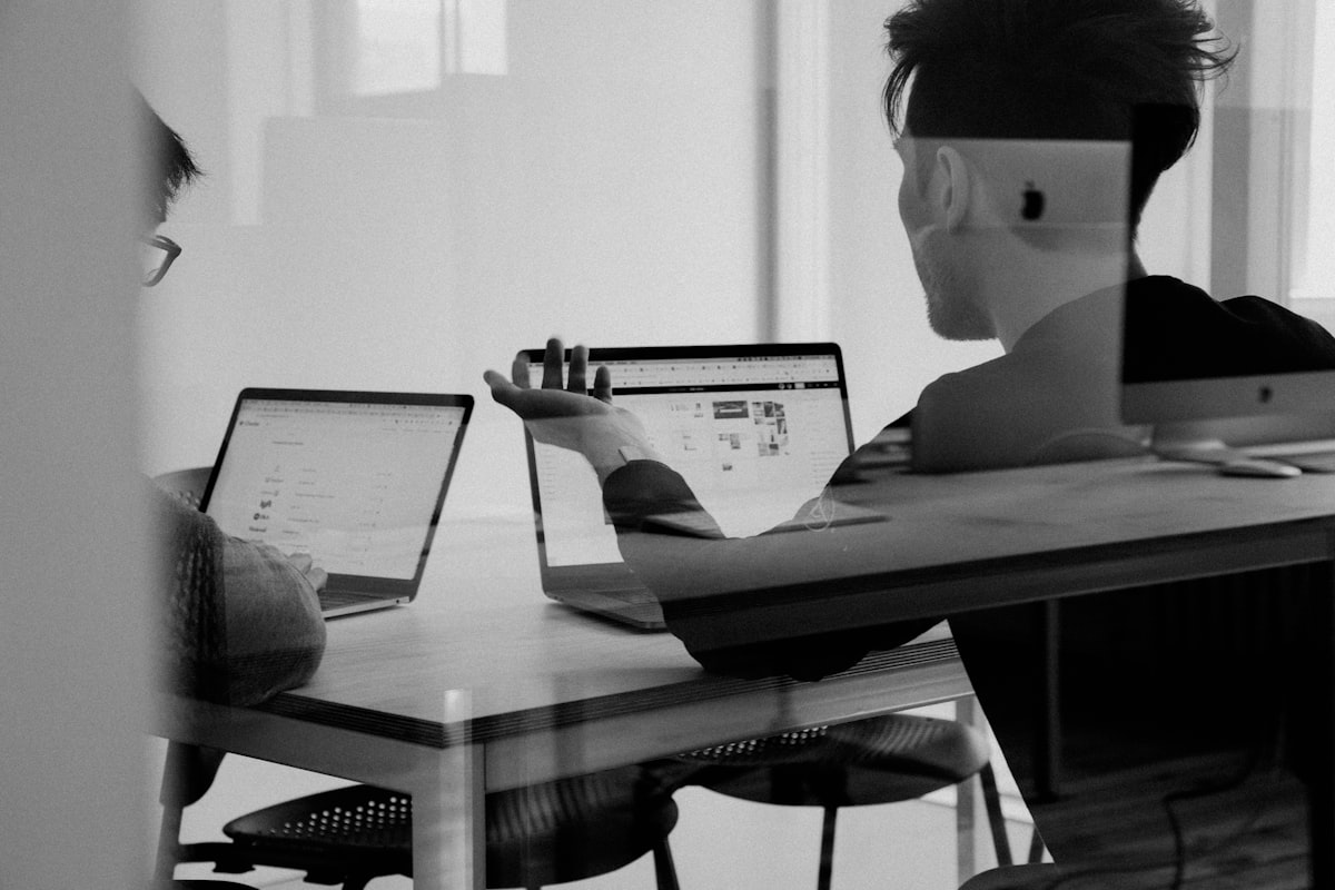 Two colleagues discussing ideas at their laptops in a modern workspace